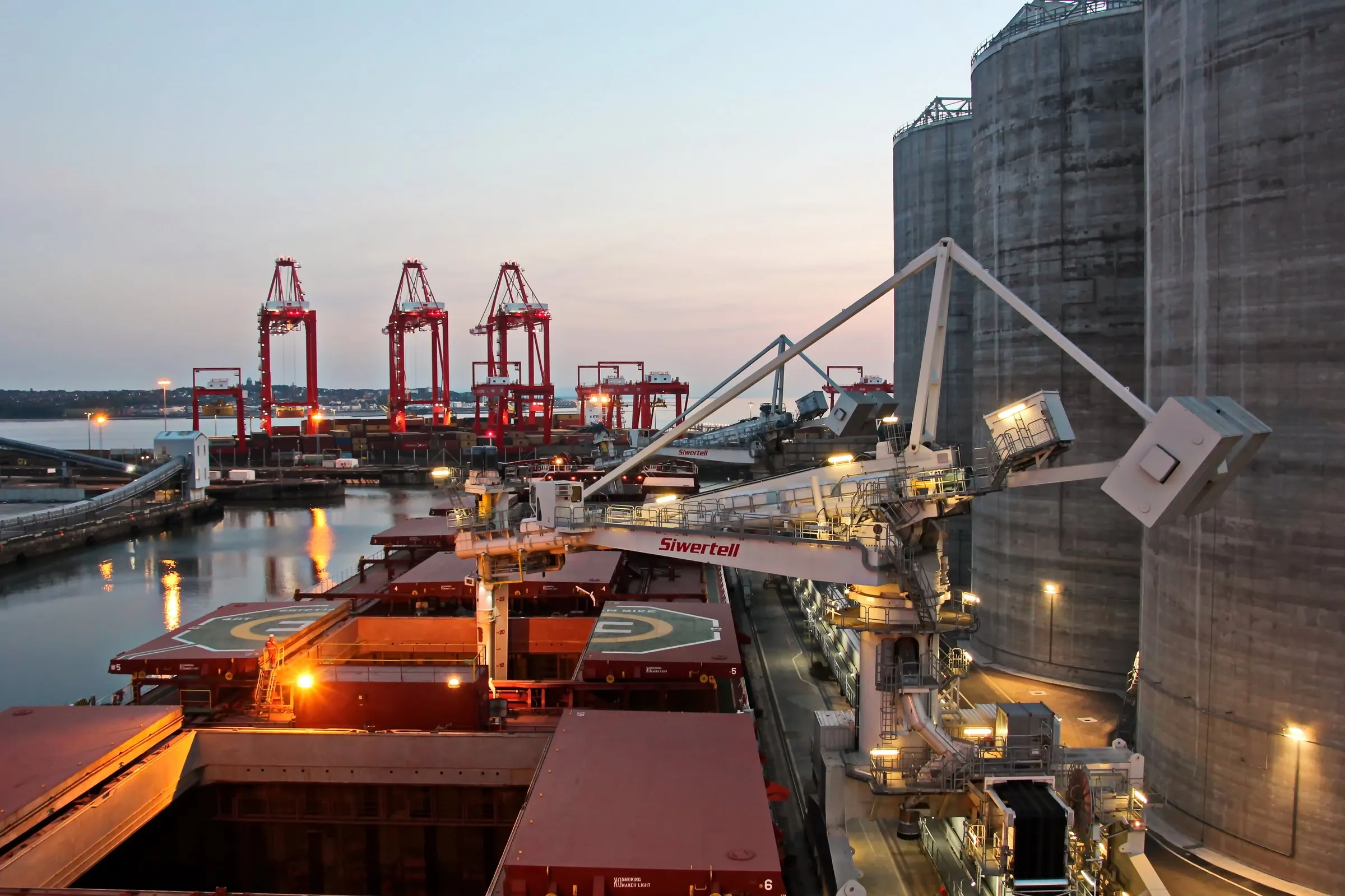 Dry-bulk vessel discharging at a port terminal at dusk.